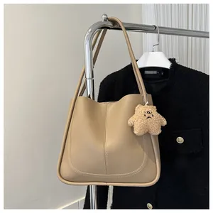 Detail of khaki leather tote bag with stylish stitching and a cute plush bear charm