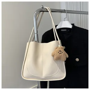 Detail of cream PU tote bag with U-shaped stitching and cute brown plush bear charm