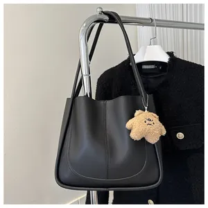 Close-up of black PU leather tote bag with vertical stitching and plush charm decoration