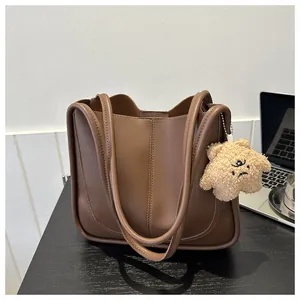 Detail of a brown PU leather tote bag with cylinder piping and a plush bear pendant