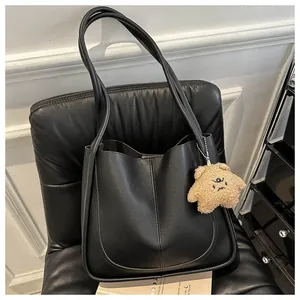 Detail of black PU leather tote bag with a beige star plush charm on a luxury leather seat