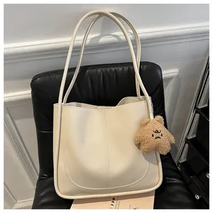 Close-up of beige PU leather tote bag with a brown plush bear charm on a black chair