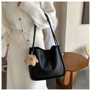 Close-up of black leather tote bag with vertical stitching and brown bear charm