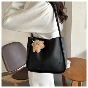 Close-up of black PU leather tote bag with U-shaped stitching and cute plush bear charm