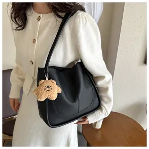Detail of black matte PU leather tote bag with curved stitching and plush bear charm