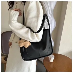 Detail of high-quality black PU leather tote bag with a cute brown teddy bear charm attached