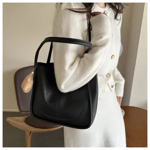 Detail of black PU leather tote bag featuring sleek stitching and a plush bear charm