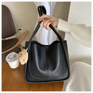 Detail of minimalist black PU leather tote bag with U-stitch and plush bear charm decoration