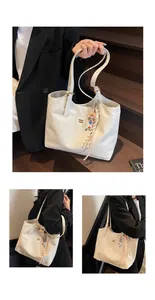 Detail view of cream tote bag featuring golden brand logo and cute cartoon charm accent