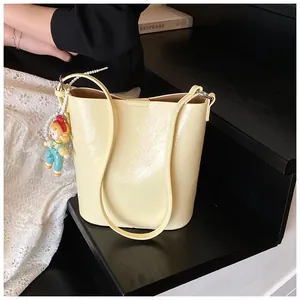 Detail of cream bucket bag showing MUDUO logo and pearl chain doll pendant