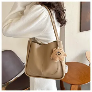 Detail view of khaki PU leather tote bag with plush bear charm and stitched seam detail