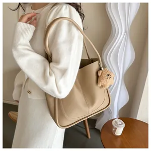 Detail view of large beige tote bag on shoulder with cute brown plush bear charm