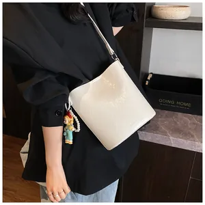 Detail of white minimalist bucket bag with litchi texture and pearl doll charm
