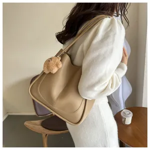 Side view of beige PU tote bag with plush bear charm on a female model shoulder