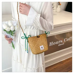 Close-up of handmade woven straw bucket bag with green braided strap and bead charms