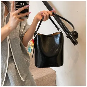 Detail of black glossy bucket bag with pearl charm and smooth leather finish