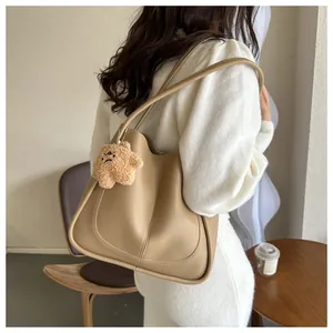 Detail view of khaki PU leather tote bag featuring stitching and a plush bear charm