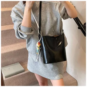 Detail of black glossy bucket bag featuring a pearl chain and cute cartoon charm