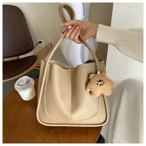 Detail of khaki tote bag featuring smooth PU leather texture and cute plush bear charm
