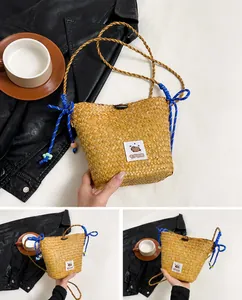 Detail of straw woven bucket bag with blue bow handles and capybara patch decoration