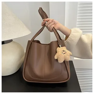 Detail of deep brown PU leather tote bag featuring a cute beige teddy bear charm