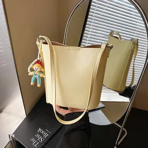 Minimalist beige leather bucket bag with litchi texture and a pearl doll pendant
