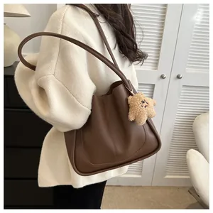 Detail view of deep brown faux leather tote bag with a beige star plush charm on model