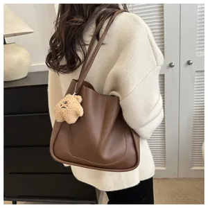 Detail of deep brown matte leather tote bag featuring a cute plush bear charm accessory