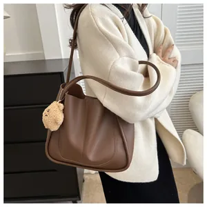 Detail of dark brown PU leather tote bag with stylish bear pendant on model side