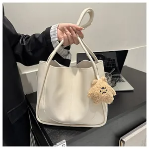 Detail of off-white PU tote bag showing leather stitching and brown plush bear charm