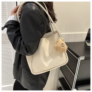 Detail of cream PU leather tote bag featuring a cute brown plush bear charm and long strap