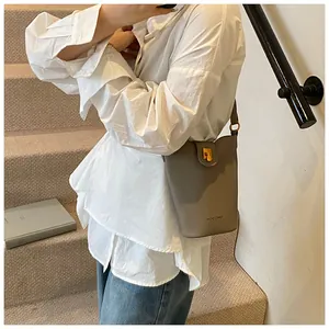 Detalle del bolso de cubo de cuero gris con cierre dorado en una escena de estilo de vida