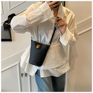 Detalle de un bolso tipo cubo de cuero negro con cierre dorado en una modelo