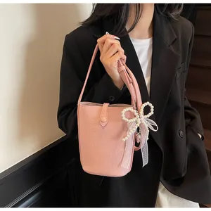 Détail du sac seau rose grainé avec pendentif nœud en perles et ruban en dentelle