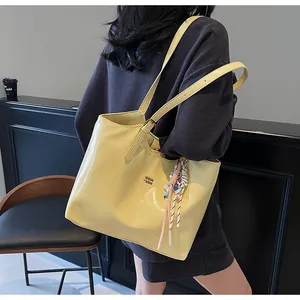 Detail of light yellow tote bag with smooth texture, gold hardware, and silk scarf accent