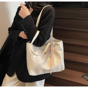 Detail of a large cream tote bag featuring a glossy finish and colorful tassel charms