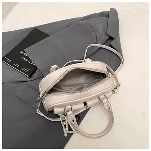 Flat lay of cream Boston bag with pearl charm on a grey blazer and magazine