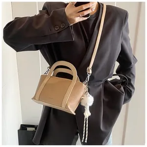 Dettaglio della borsa a secchiello beige con trama litchi, ciondolo peluche e manici in pelle