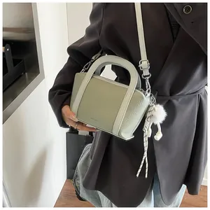 Dettaglio borsa a secchiello verde chiaro in pelle litchi con pompon bianco e tracolla