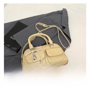 Detail of cream Boston bag with pearl bow charm and dual front pockets with silver hardware