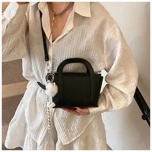 Dettaglio della borsa in pelle nera a grana con pompon bianco e ciondolo in corda intrecciata