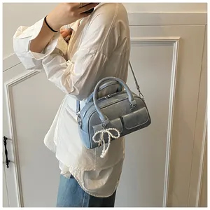 Detail of light blue glossy Boston bag featuring front pockets and pearl bow charm