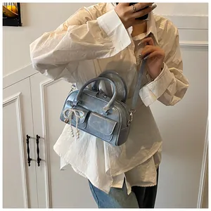 Detail of light blue Boston bag with dual handles and pearl bow charm on model