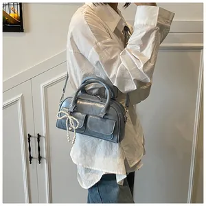 Detail of blue Boston bag with glossy texture and pearl bow charm on white shirt
