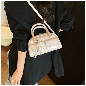 Detail shot of pearl white Boston bag with bow charm and front pocket features