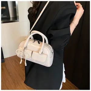 Side view of cream Boston bag with pearl bow charm and twin handles on a model
