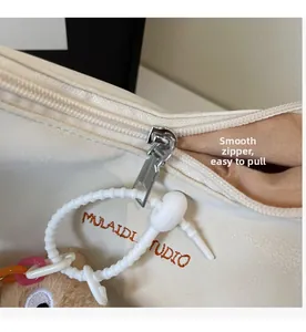 Détail du zip argenté fluide et du pendentif ours en peluche sur un sac blanc