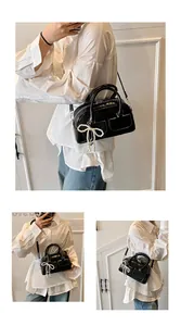 Detail of black glossy Boston bag featuring pearl bow charm and dual front pockets