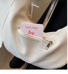 Gros plan de la poche latérale zippée sur un sac hobo beige montrant l'espace de rangement