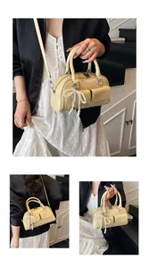 Detail view of cream Boston bag with pearl bow charm and adjustable strap on a model
